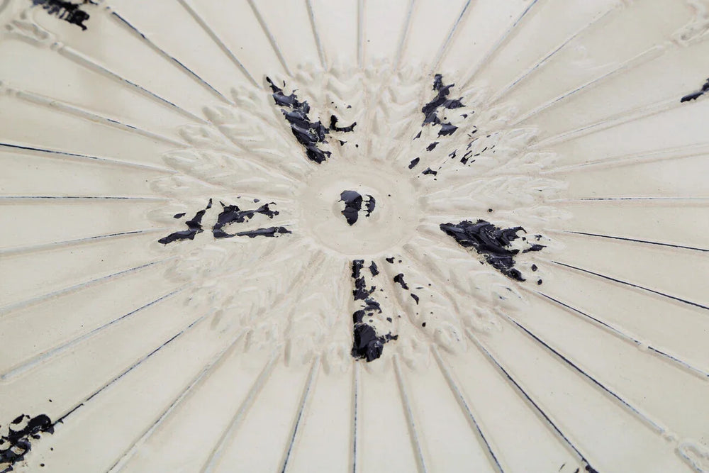 Close view of cream ceramic table top with embossed floral pattern and distressed finish