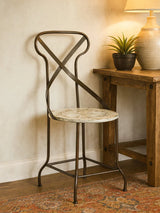 Metal accent chair with cross back and round patterned seat beside a wooden side table