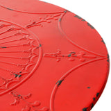 Close-up view of a round red metal bar table featuring an intricate embossed design on the surface, showcasing floral and geometric patterns with a distressed finish