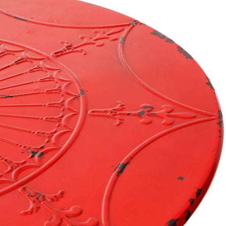 Close-up view of a round red metal bar table featuring an intricate embossed design on the surface, showcasing floral and geometric patterns with a distressed finish