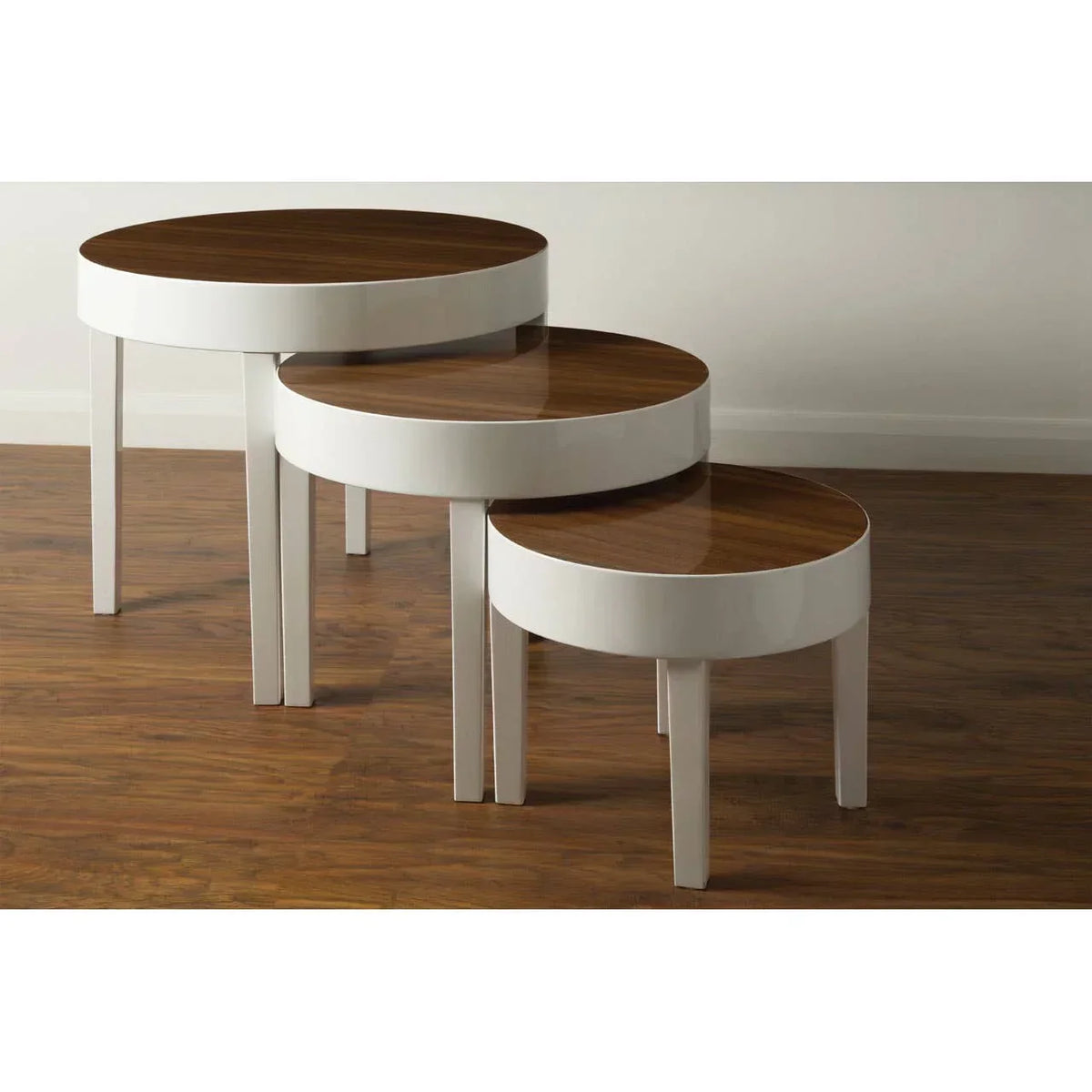 Set of three round nesting tables with white legs and walnut tops on wood floor
