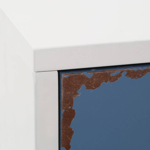 A close-up view of the Alchemy Side Table showcasing a sleek, modern design with a white frame and a dark blue surface featuring a textured edge. The corner of the table is highlighted, emphasizing the contrast between the materials