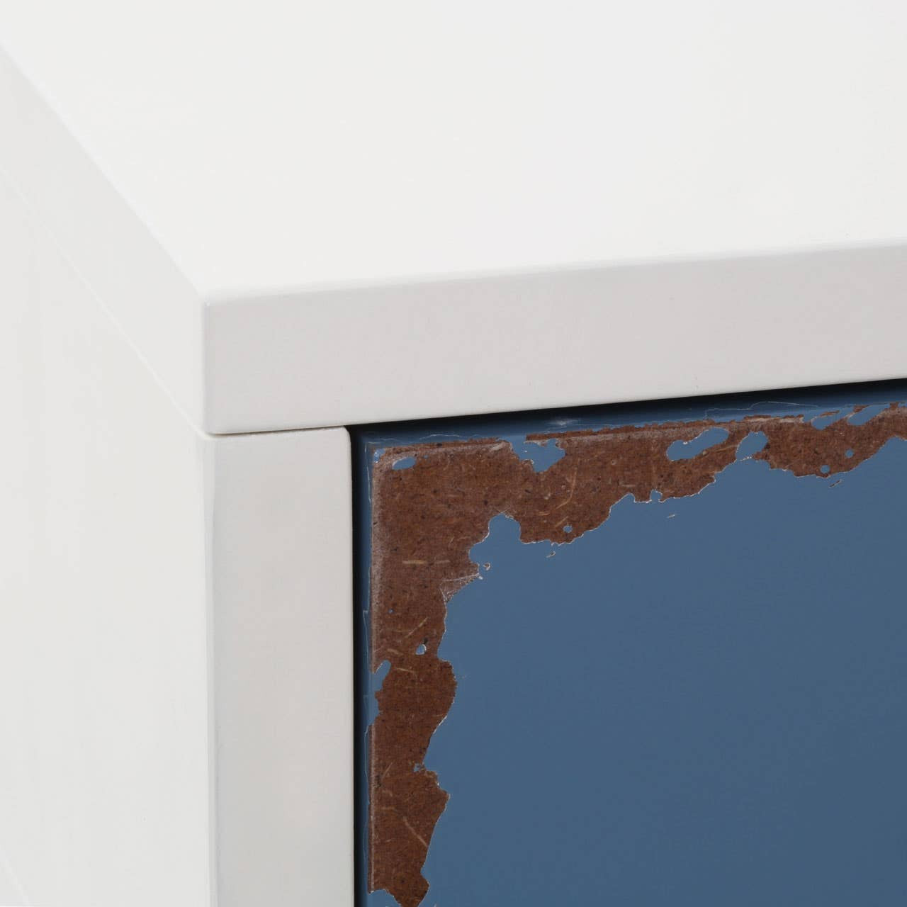 A close-up view of the Alchemy Side Table showcasing a sleek, modern design with a white frame and a dark blue surface featuring a textured edge. The corner of the table is highlighted, emphasizing the contrast between the materials