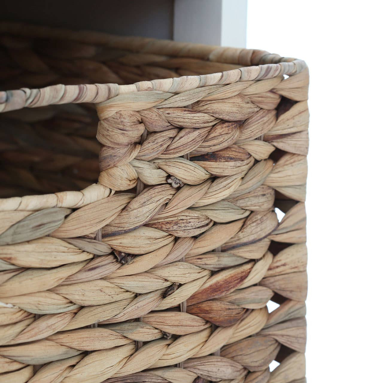 Close-up view of a woven basket with a natural texture, showcasing the intricate design and open handle. The basket is part of a cabinet featuring two drawers and four similar baskets, designed for home storage. The cabinet has a light ivory finish, complementing the earthy tones of the basket