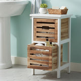 Two-drawer chest featuring a white frame and natural wood accents, with slatted design on the drawers. The top drawer is slightly smaller and has a decorative basket on top, while the bottom drawer is larger and open, displaying toiletries. The chest stands on four legs against a light blue wall, with a sink visible in the background