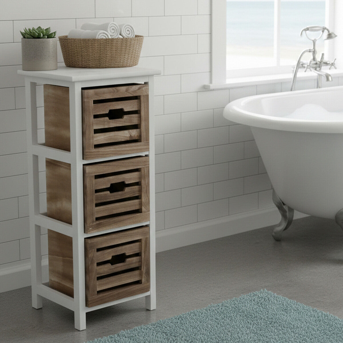 Three-drawer chest with a white frame and natural woven baskets, placed beside a freestanding bathtub in a bright bathroom setting. A decorative bowl sits on top of the chest, and a soft blue rug is visible on the floor