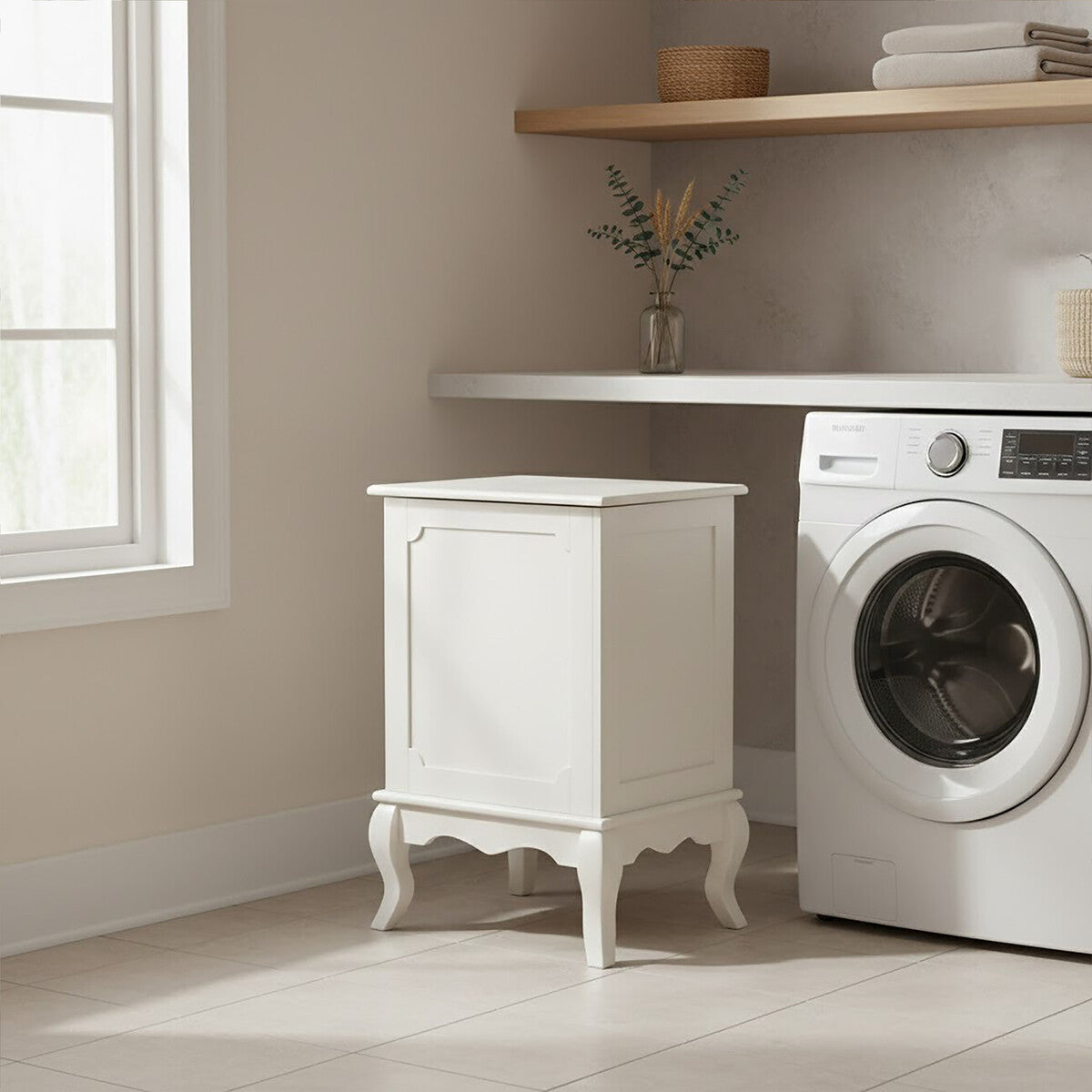 Ivory finish laundry hamper with a lift-up lid, featuring decorative paneling and elegant curved legs, positioned next to a washing machine in a bright laundry room with natural light streaming through a window and a wooden shelf above