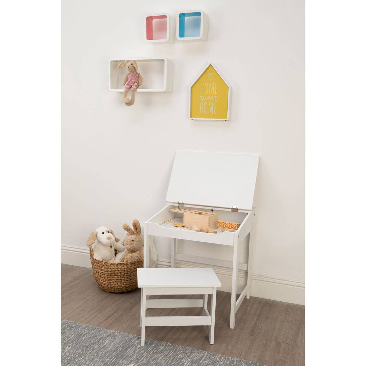 Three white floating wall cubes are mounted on a light-colored wall, displaying decorative items. Below, a white chair with a lift-top seat is positioned next to a small white step stool. A woven basket filled with soft toys sits on the floor, adding a cozy touch to the space