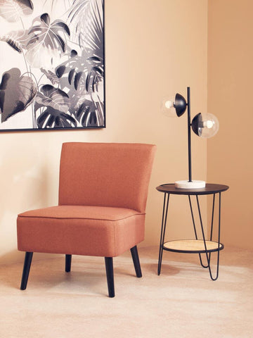 Rust accent chair with black legs beside round side table and modern table lamp