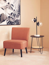 Rust accent chair with black legs beside round side table and modern table lamp
