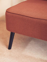 Close-up of rust fabric sofa corner with tapered black wooden leg on beige carpet