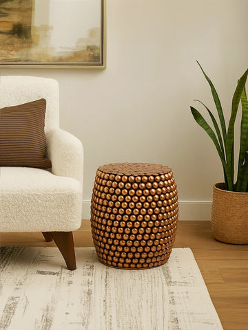 A copper finish barrel stool with a textured pattern sits next to a cream-colored sofa on a light rug, with a potted plant in the background