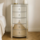 Verona Curved Tall Boy Drawers featuring a sleek mirrored finish, five curved drawers with circular handles, and a stylish design that enhances modern home decor. The unit stands on a wooden floor beside a light-colored bed with neutral bedding