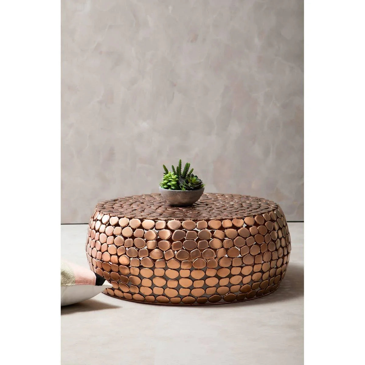 Round copper coffee table with textured surface and small plant decor