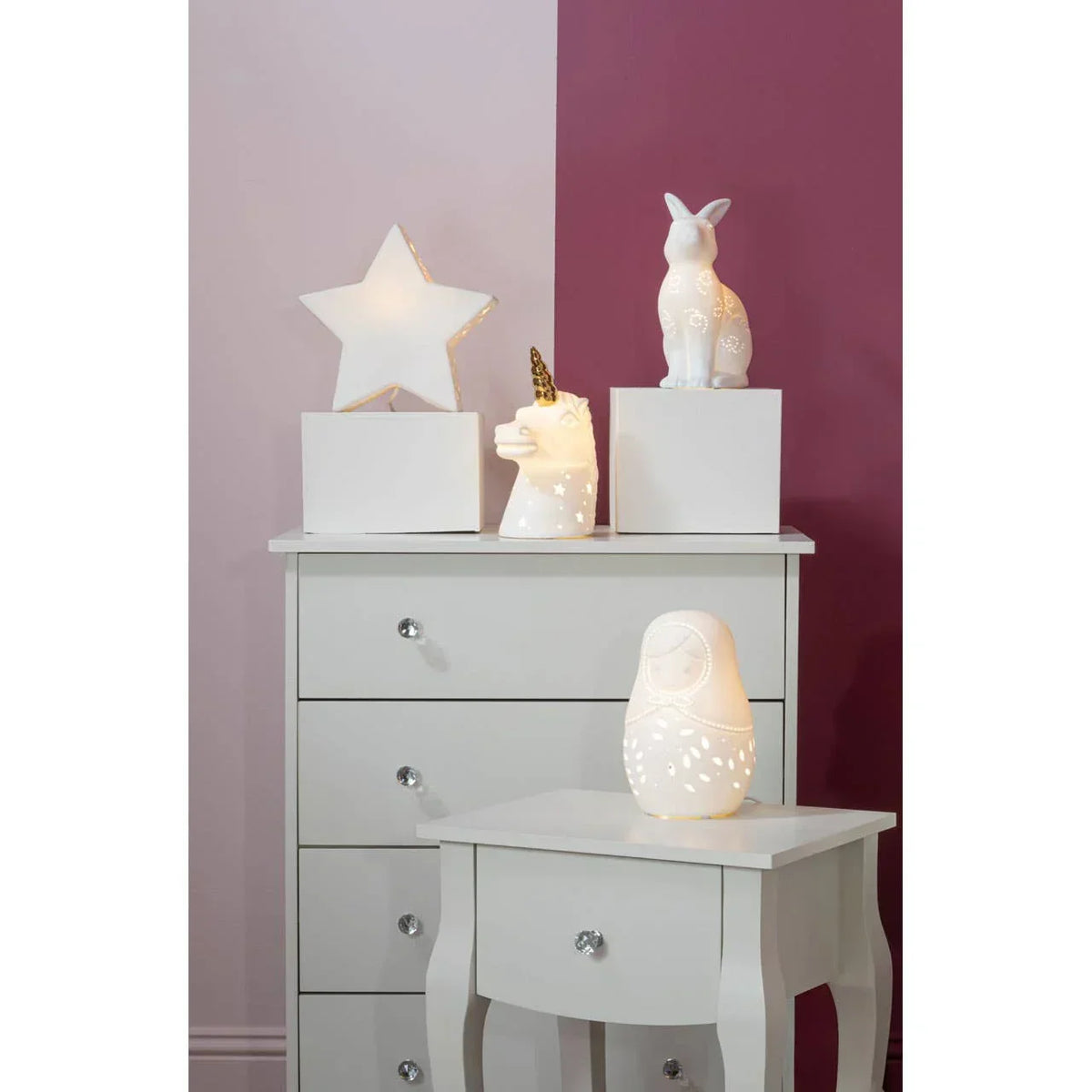 Ceramic animal and star shaped novelty lamps on white bedroom furniture against two-tone wall