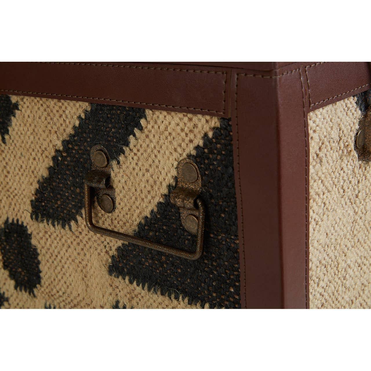 Closeup of storage trunk with geometric jute weave, brown leather trim and metal handle