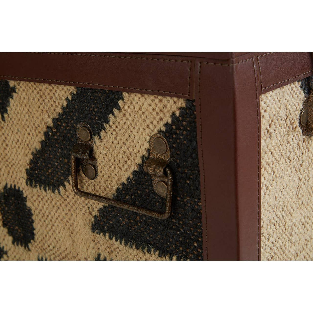 Closeup of storage trunk with geometric jute weave, brown leather trim and metal handle