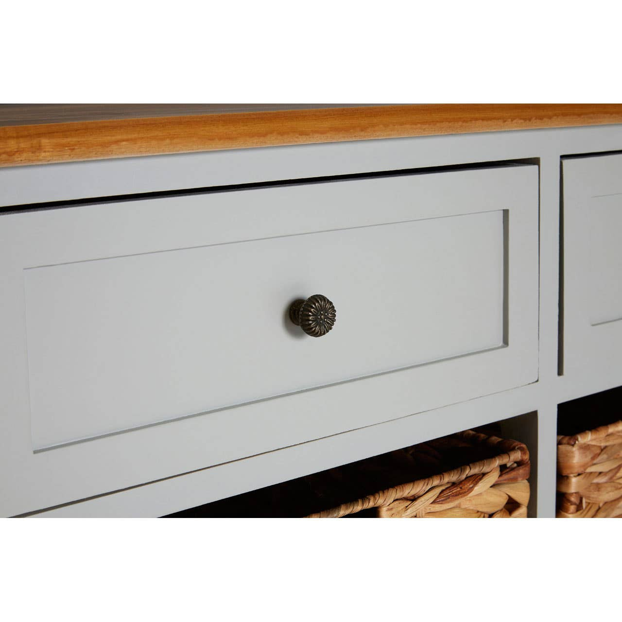 The Vermont Two Drawers Four Baskets Cabinet features a light gray finish with a smooth wooden top. It includes two spacious drawers with round bronze knobs and four woven baskets below, providing stylish storage options. The cabinet has clean lines and a modern design, suitable for various home decor styles