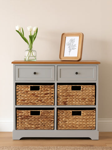 A gray cabinet with a wooden top featuring two upper drawers and four woven baskets below. The cabinet is styled against a light-colored wall, with a vase of white flowers and a framed picture placed on top