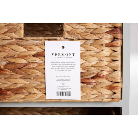 The Vermont Two Drawers Four Baskets Cabinet features a natural woven texture on the baskets, with a label attached that includes product information. The cabinet has a sleek design with a light-colored frame, showcasing the contrast between the woven baskets and the cabinet structure