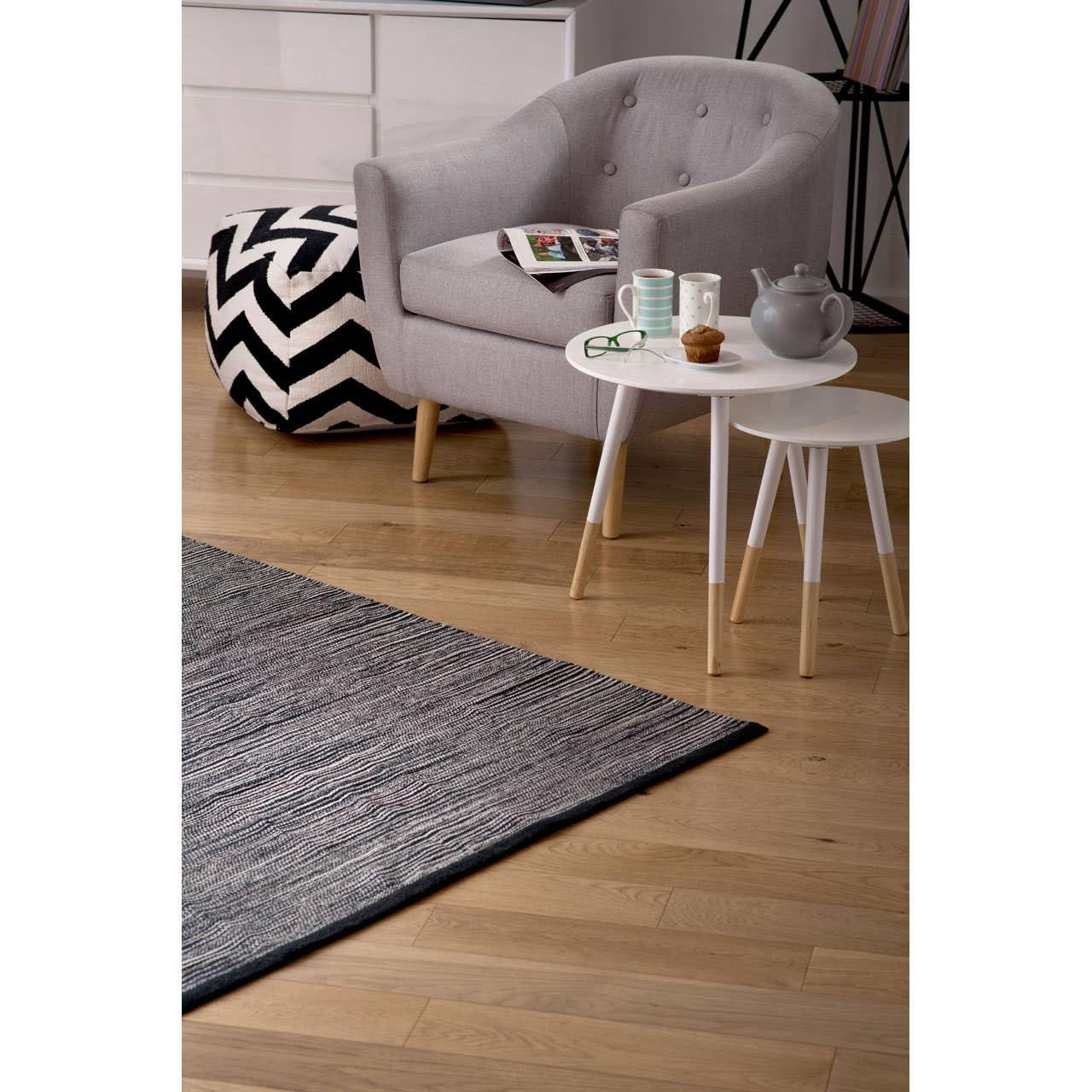 Grey armchair with wooden legs, white nesting tables and patterned pouffe on wood floor