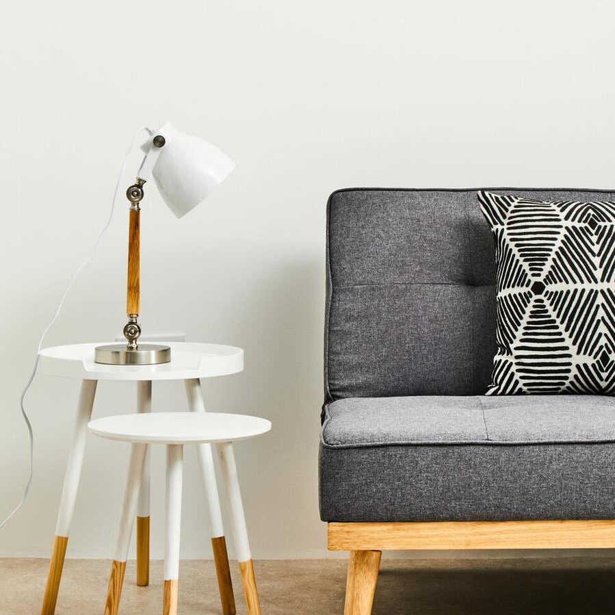 Grey fabric sofa with geometric cushion beside two white wooden nesting tables and desk lamp