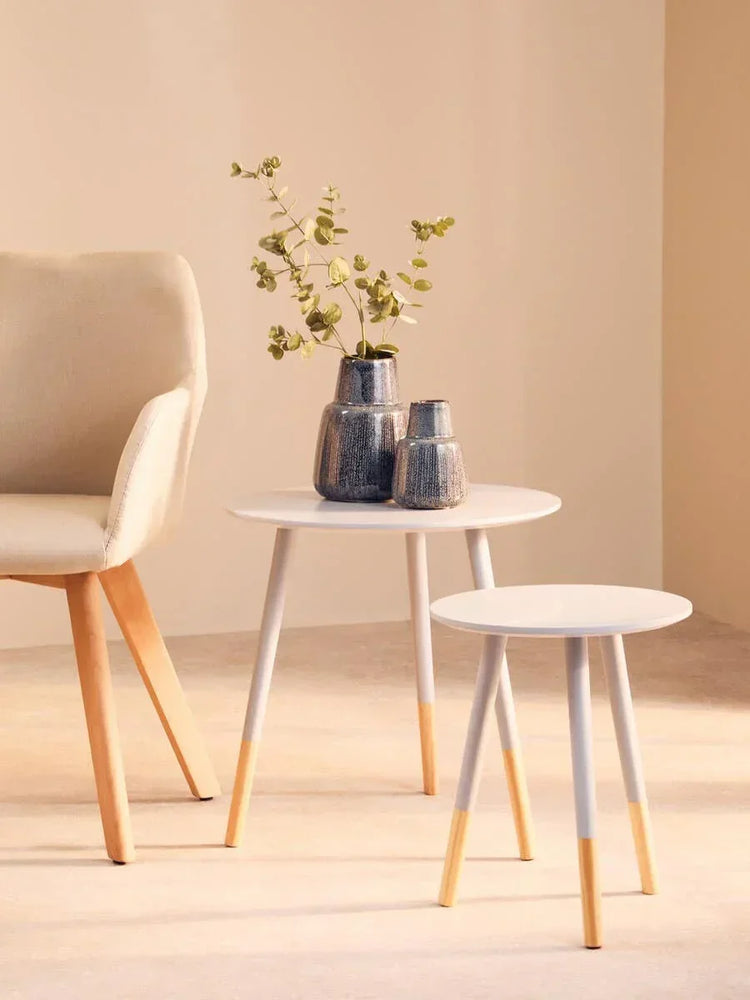 Scandi-style white nesting tables with wood legs and vases beside beige accent chair