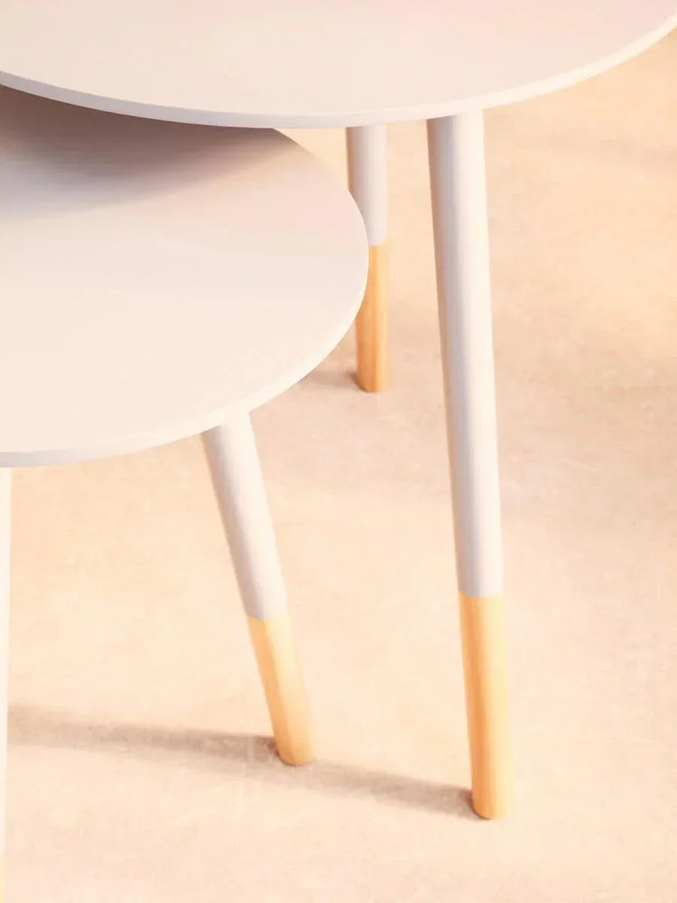 Round nesting tables with white tops and two-tone wooden legs on light floor