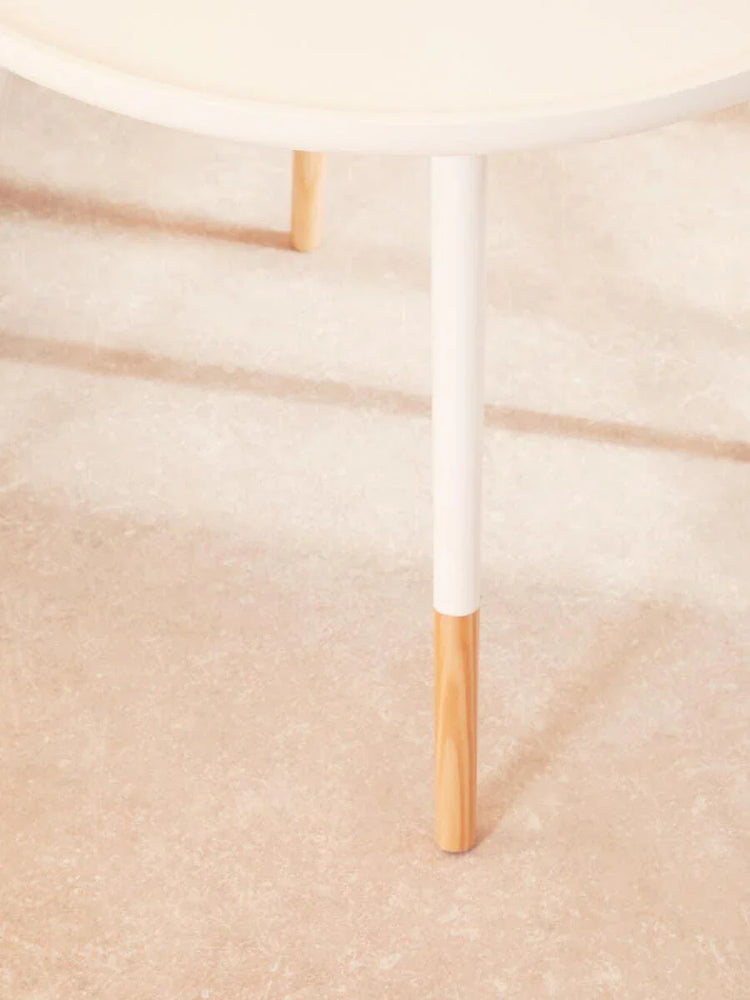 Round white coffee table with wooden dipped legs on light textured floor