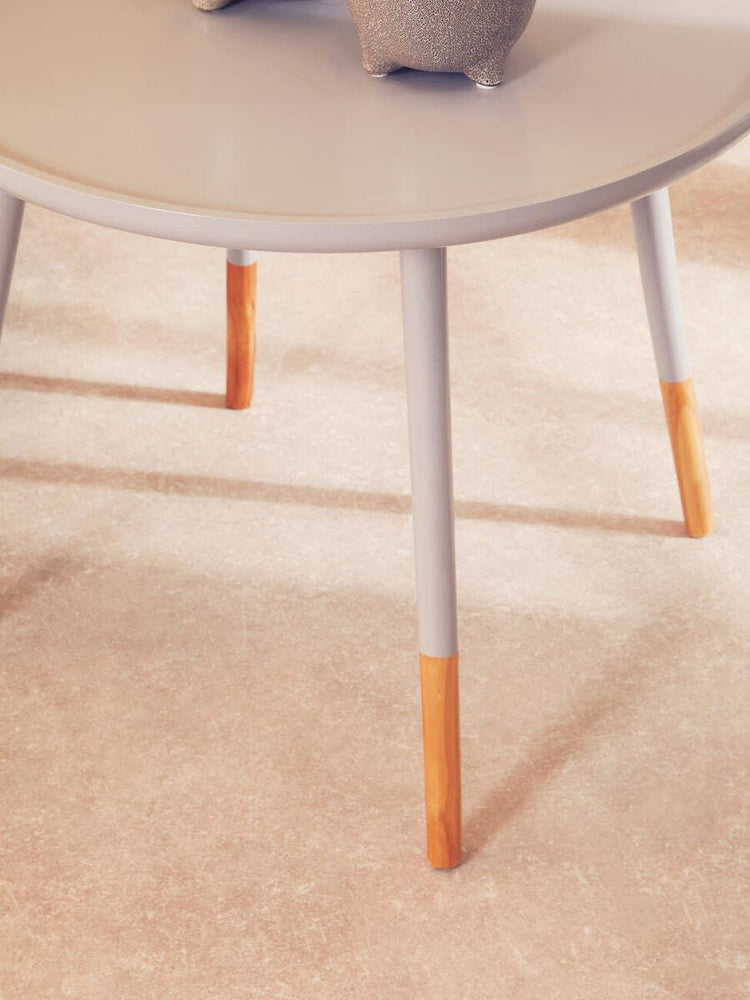 Round grey coffee table with wooden leg tips on beige floor, ceramic planter on top