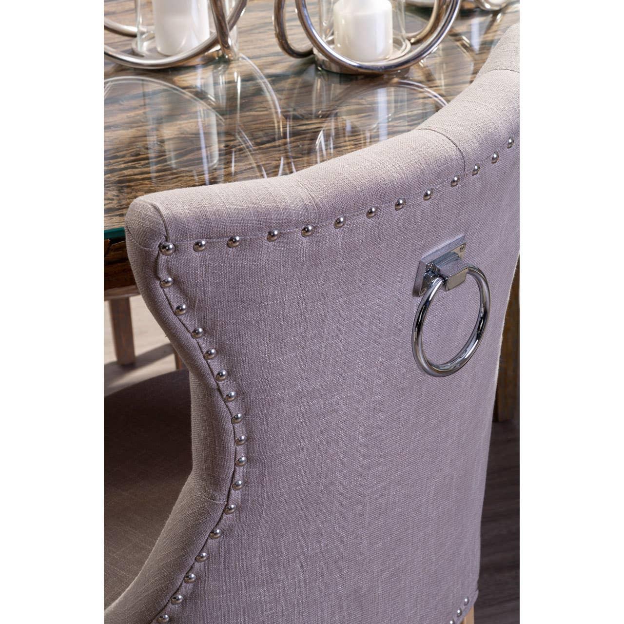 Grey upholstered dining chair with chrome ring handle and studded trim at glass table