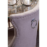 Grey upholstered dining chair with chrome ring handle and studded trim at glass table