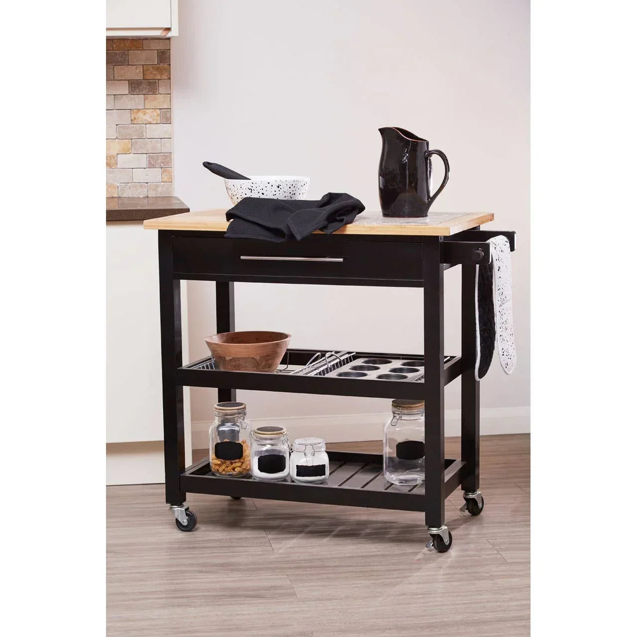 Black kitchen trolley with wooden top, storage shelves, and jars in a modern kitchen