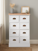 A white chest of drawers with eight drawers, featuring a natural wood top and simple cut-out handles, placed against a light gray wall. A small decorative frame and a vase with dried flowers are positioned on the top surface