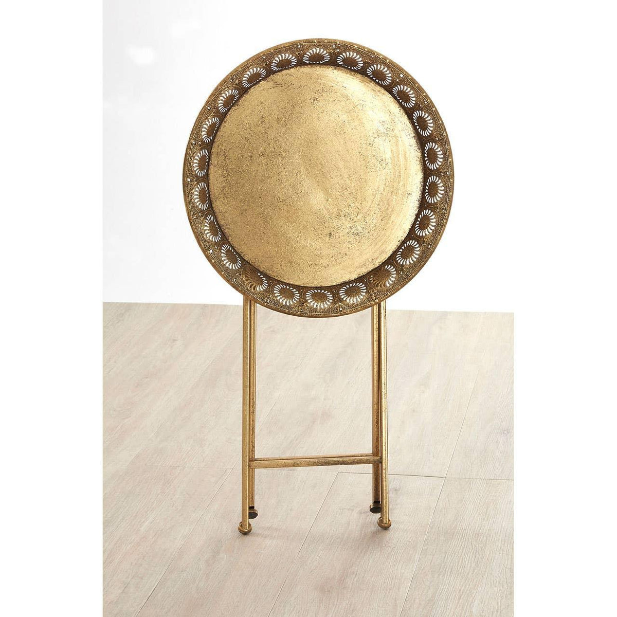 Round gold metal tray table with decorative cut-out pattern, standing on folding legs
