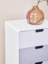 A white chest of four drawers with a smooth finish, featuring three drawers in a light color and one drawer in a darker shade. A decorative glass vase sits on top, showcasing a minimalist design. The background is a soft, neutral color, enhancing the modern aesthetic of the furniture piece