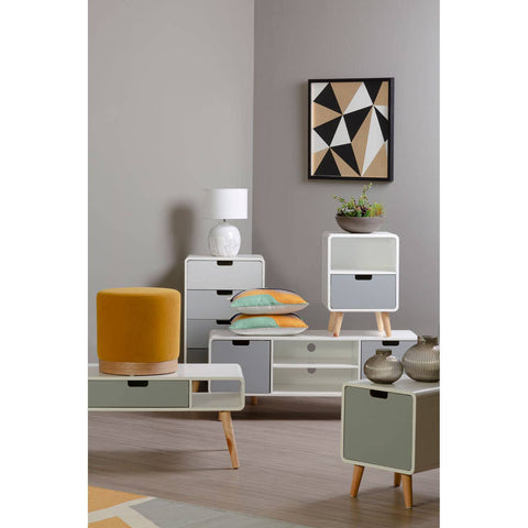 Milo Chest of 4 Drawers featuring a modern design with a light wood finish, four spacious drawers with sleek black handles, and tapered wooden legs. The chest is positioned in a stylish room setting with a geometric wall art piece, a small potted plant, and a lamp on top, complemented by colorful cushions and a cozy chair nearby