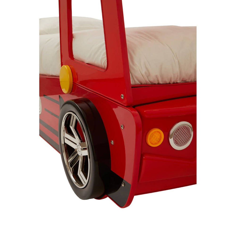 A close-up view of the corner of a red fire engine bed for kids, featuring a black wheel with silver detailing and a bright red body. The bed has a soft, white mattress visible in the background, with a playful design that resembles a fire truck