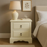 Cream bedside table with two drawers, lamp, book, and glass of water beside a bed