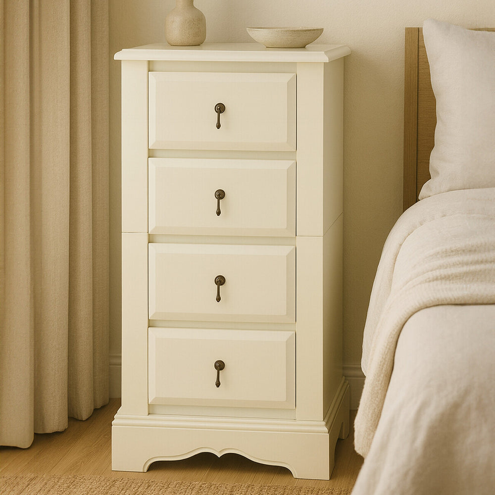 Florence Ivory Chest of 4 Drawers featuring a smooth, light ivory finish, four spacious drawers with decorative keyhole handles, and a slightly curved base, positioned beside a bed with a neutral-colored blanket and curtains in the background