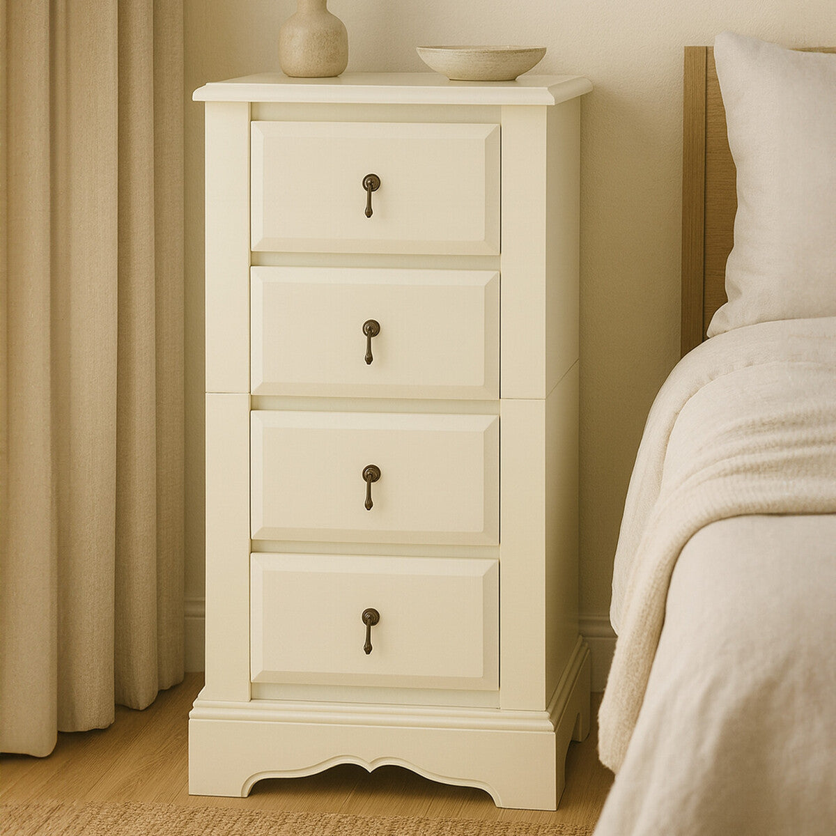 Florence Ivory Chest of 4 Drawers featuring a smooth, light ivory finish, four spacious drawers with decorative keyhole handles, and a slightly curved base, positioned beside a bed with a neutral-colored blanket and curtains in the background