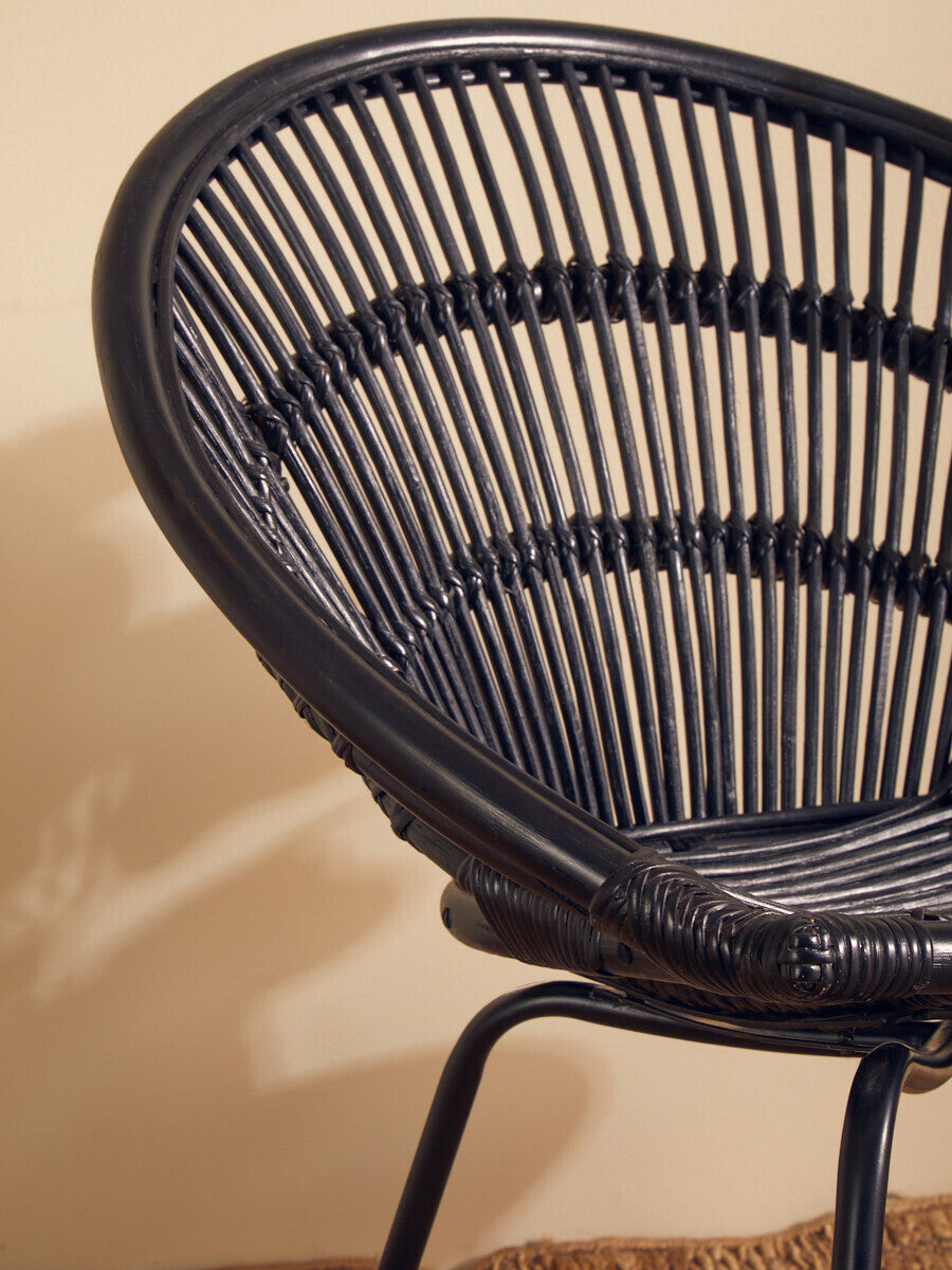 Black natural rattan chair with a curved design and iron legs, showcasing a woven texture and a modern aesthetic against a neutral background