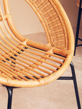 Natural rattan chair with a curved, open design and black iron legs, showcasing a blend of organic texture and modern style, set against a neutral background