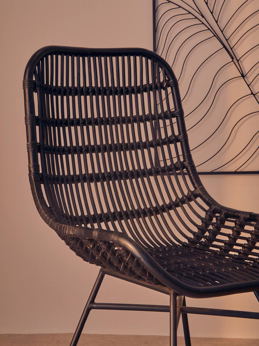 Curved black natural rattan chair with a sleek, modern design featuring horizontal and vertical woven patterns, supported by thin metal legs, set against a soft, neutral background