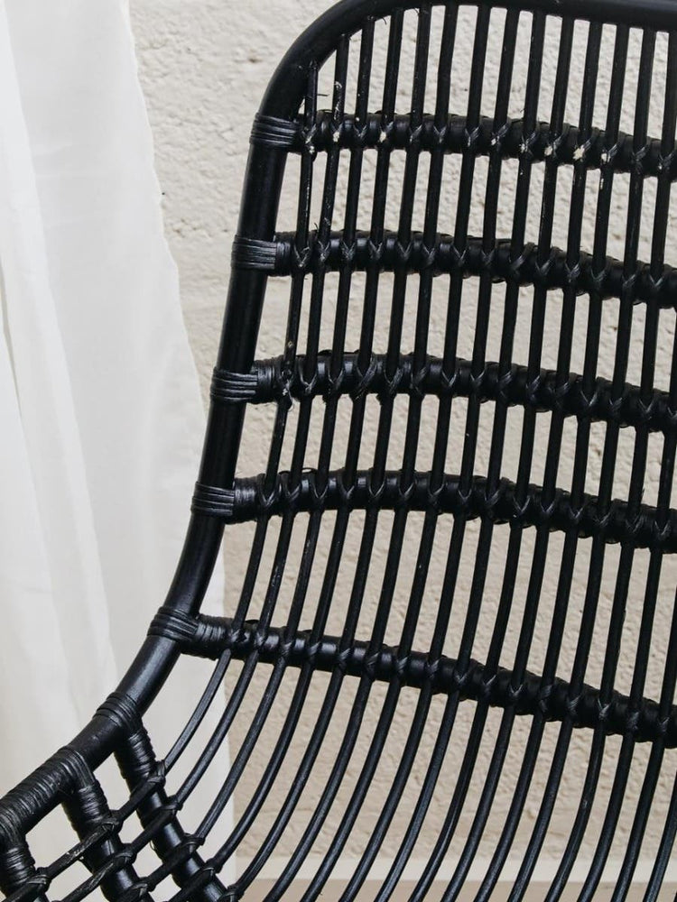 Curved black rattan chair with a sleek, modern design featuring horizontal and vertical woven patterns, showcasing a natural texture and a minimalist aesthetic. The chair's backrest is gently arched, providing a comfortable seating option