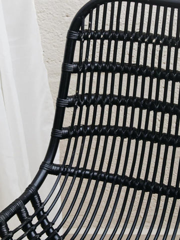 Curved black rattan chair with a sleek, modern design featuring horizontal and vertical woven patterns, showcasing a natural texture and a minimalist aesthetic. The chair's backrest is gently arched, providing a comfortable seating option
