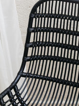 Curved black rattan chair with a sleek, modern design featuring horizontal and vertical woven patterns, showcasing a natural texture and a minimalist aesthetic. The chair's backrest is gently arched, providing a comfortable seating option