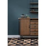 A wooden sideboard with four drawers, featuring a warm brown finish and sleek metal handles, positioned against a dark teal wall. The sideboard has an open shelf above it, displaying decorative items, and is set on a geometric patterned floor in black and beige tones