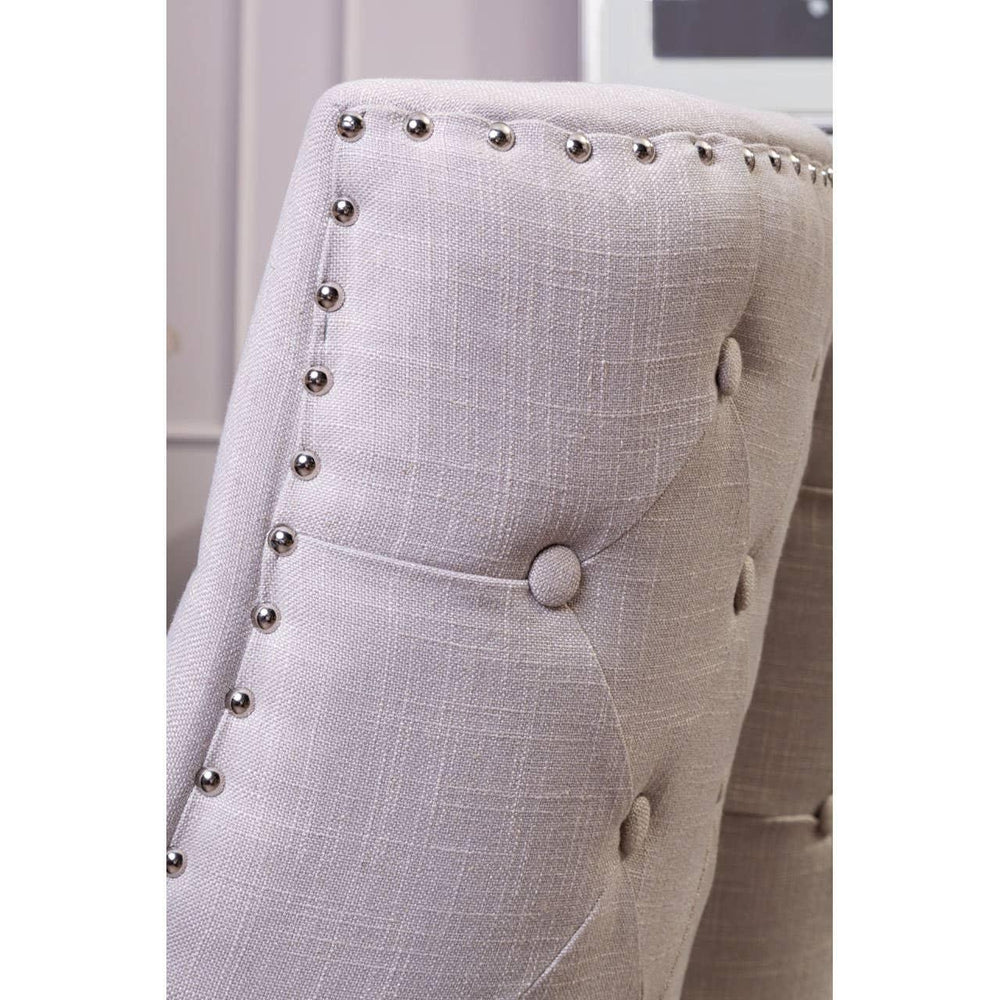 Light grey upholstered dining chair with button tufting and metal stud detailing, close view