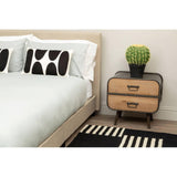 Two-drawer wooden bedside table with black metal frame beside upholstered bed and cactus plant